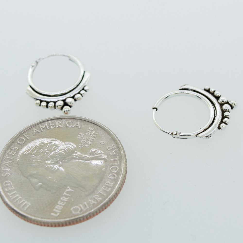 A pair of Super Silver Small Freestyle Ball Hoop earrings featuring a ball pattern design, placed next to a penny.
