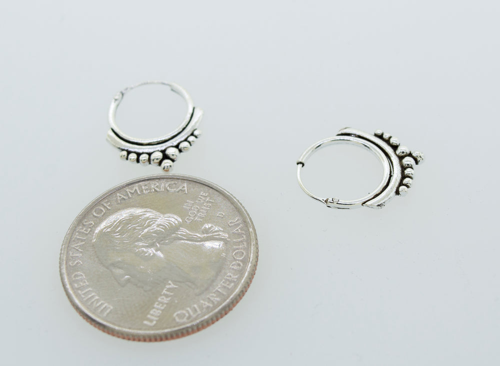 
                  
                    A pair of Super Silver Small Freestyle Ball Hoop earrings featuring a ball pattern design, placed next to a penny.
                  
                