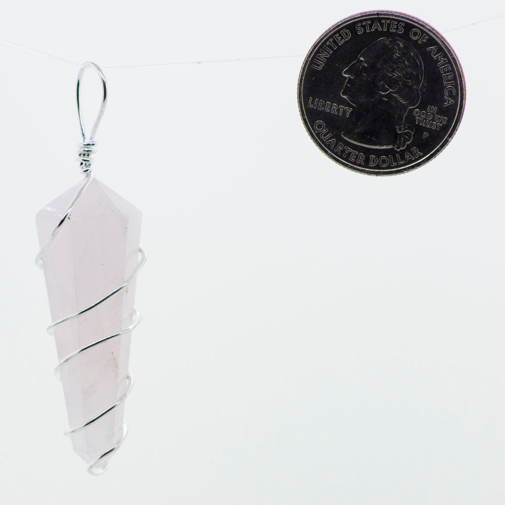 
                  
                    A Super Silver wire-wrapped rose quartz pendant hanging on a string next to a penny.
                  
                